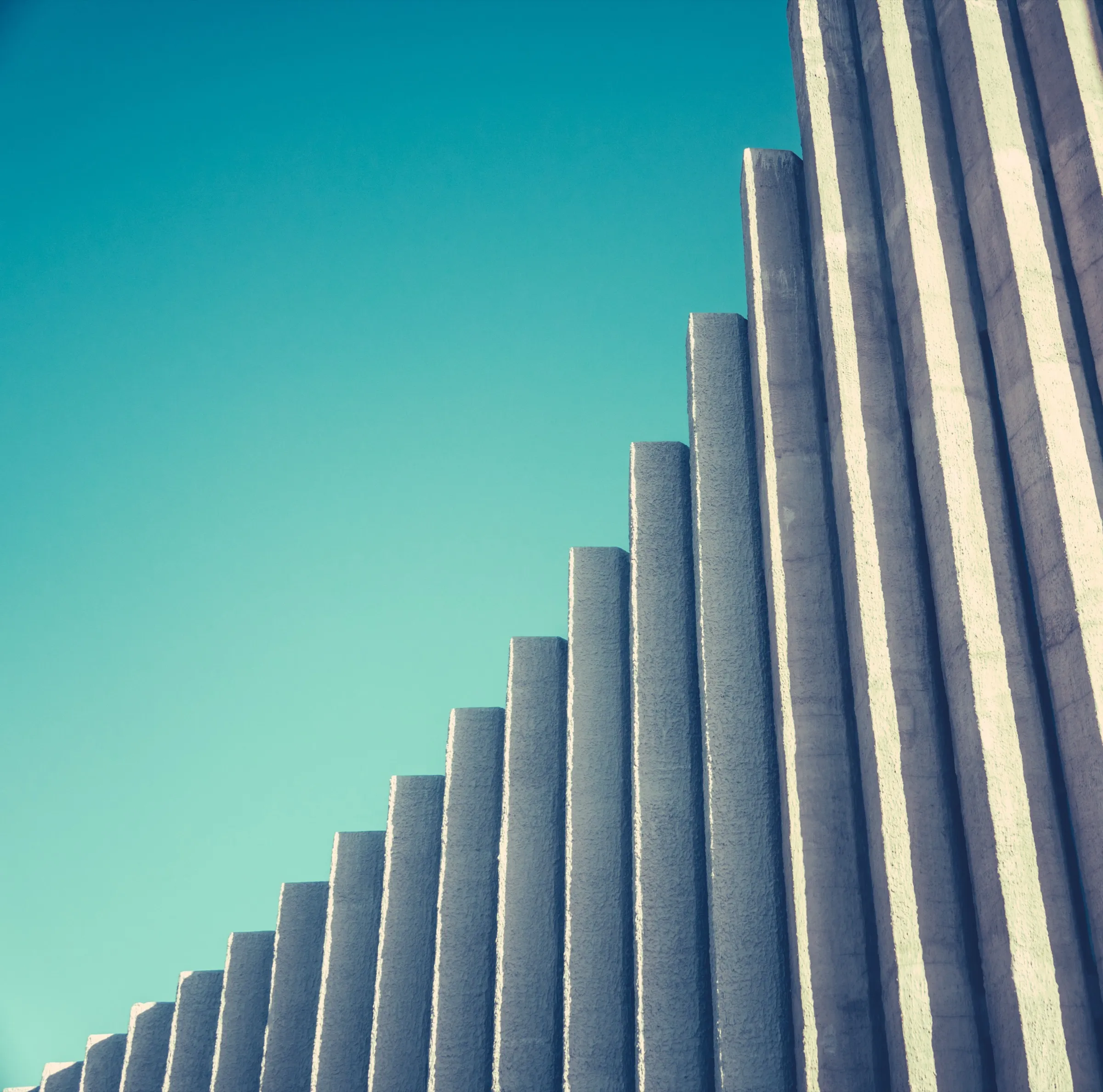Stepped concrete columns rising against a clear teal sky