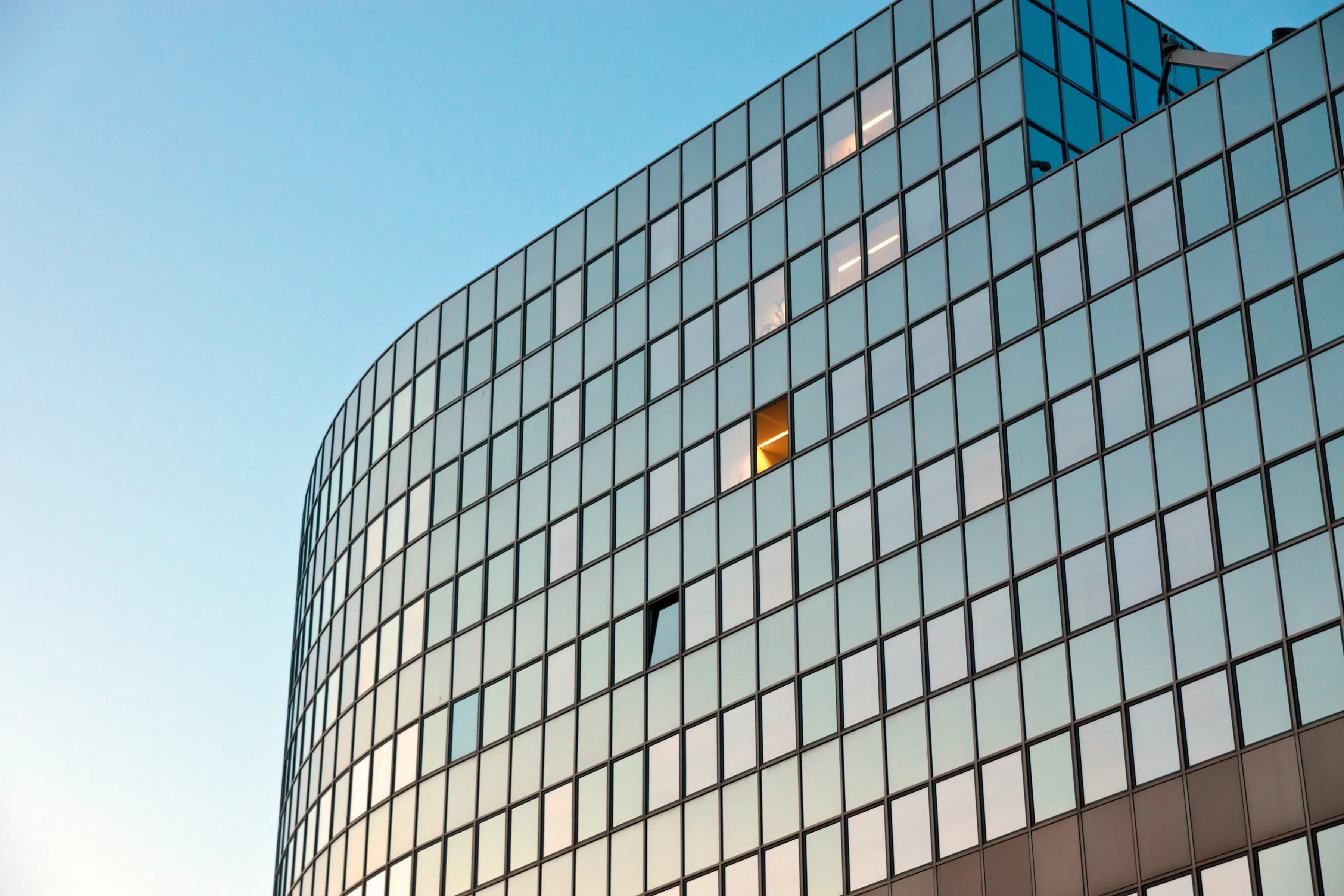 Curved glass office tower facade at dusk, reflecting the sky