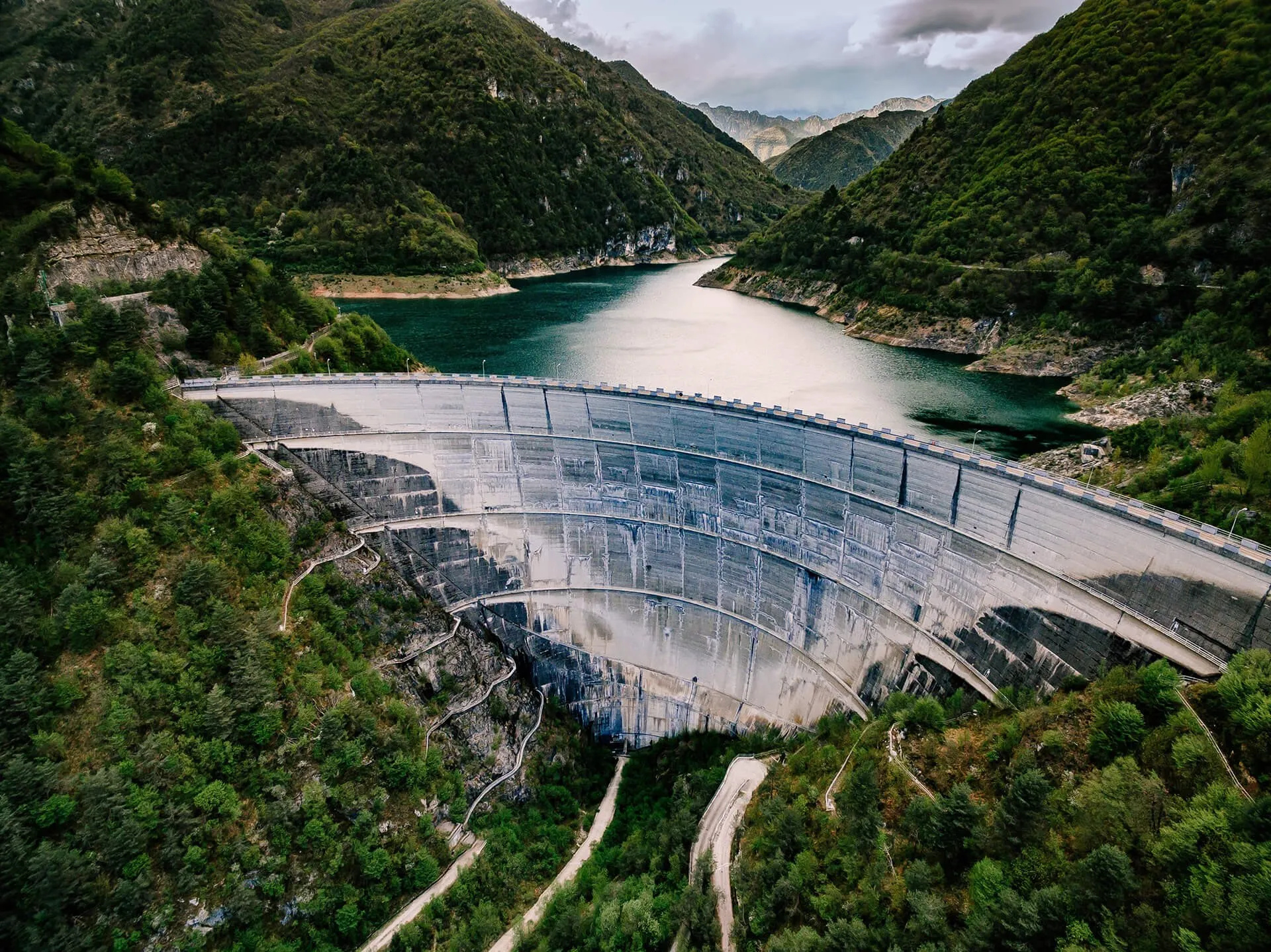Aerial view of a curved concrete arch dam holding back a green reservoir in a forested mountain valley — cover image for the Aterra Solutions website project