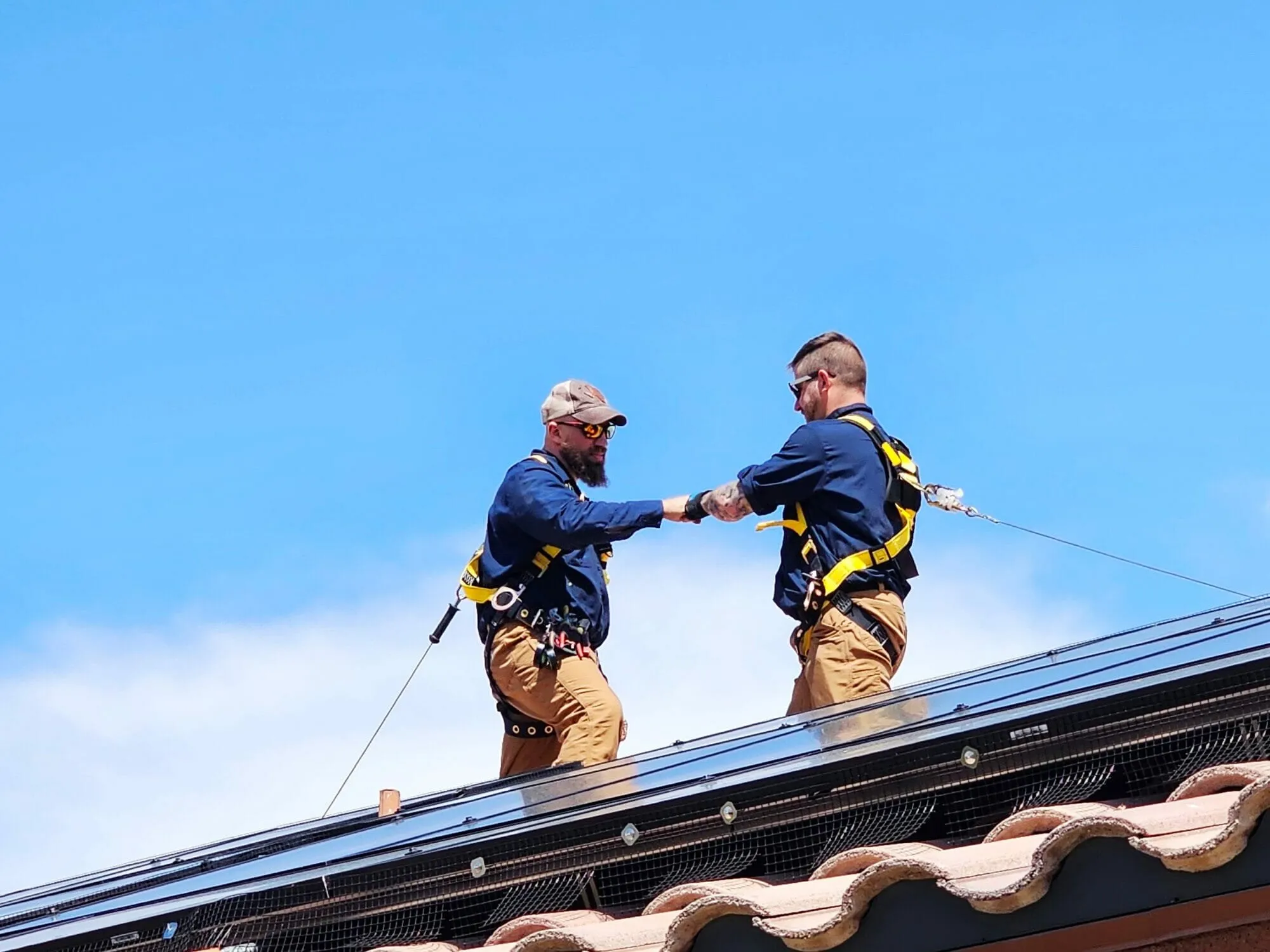 Two harnessed installers fist-bumping on a tile roof beside newly mounted solar panels — cover image for the Bob's Repair Solar website project