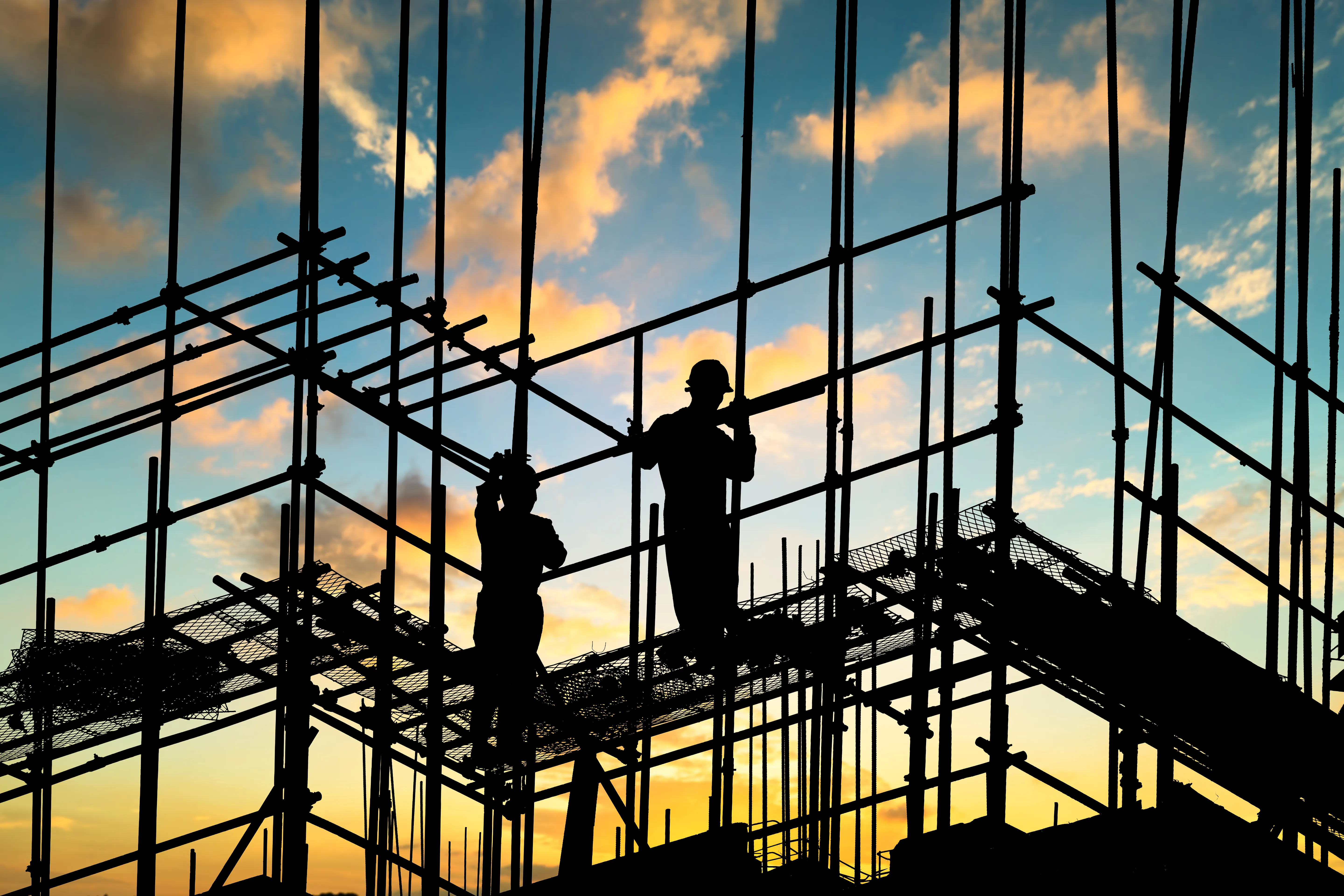 Construction workers guiding a beam into place on scaffolding at sunset