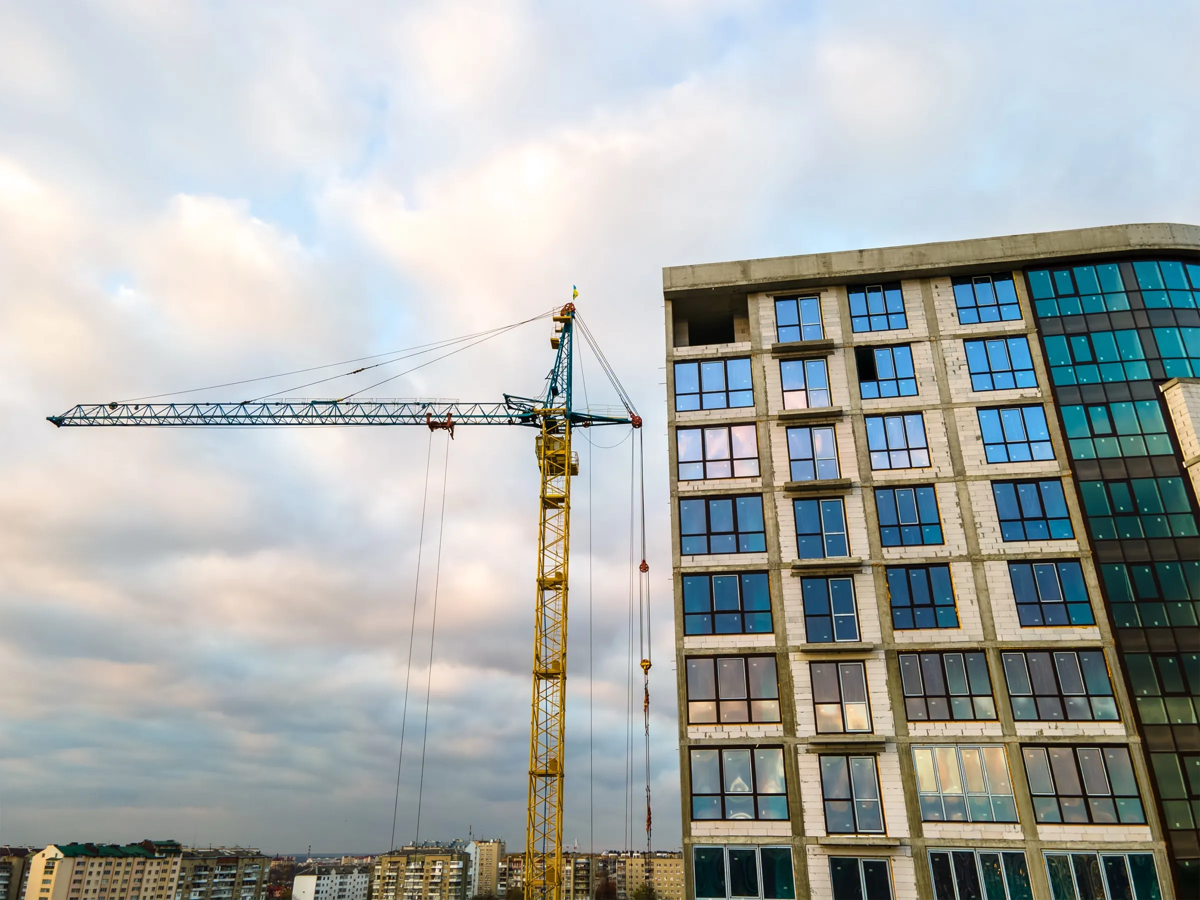 Tower crane beside a newly built mid-rise with a glass curtain wall under a cloudy sky
