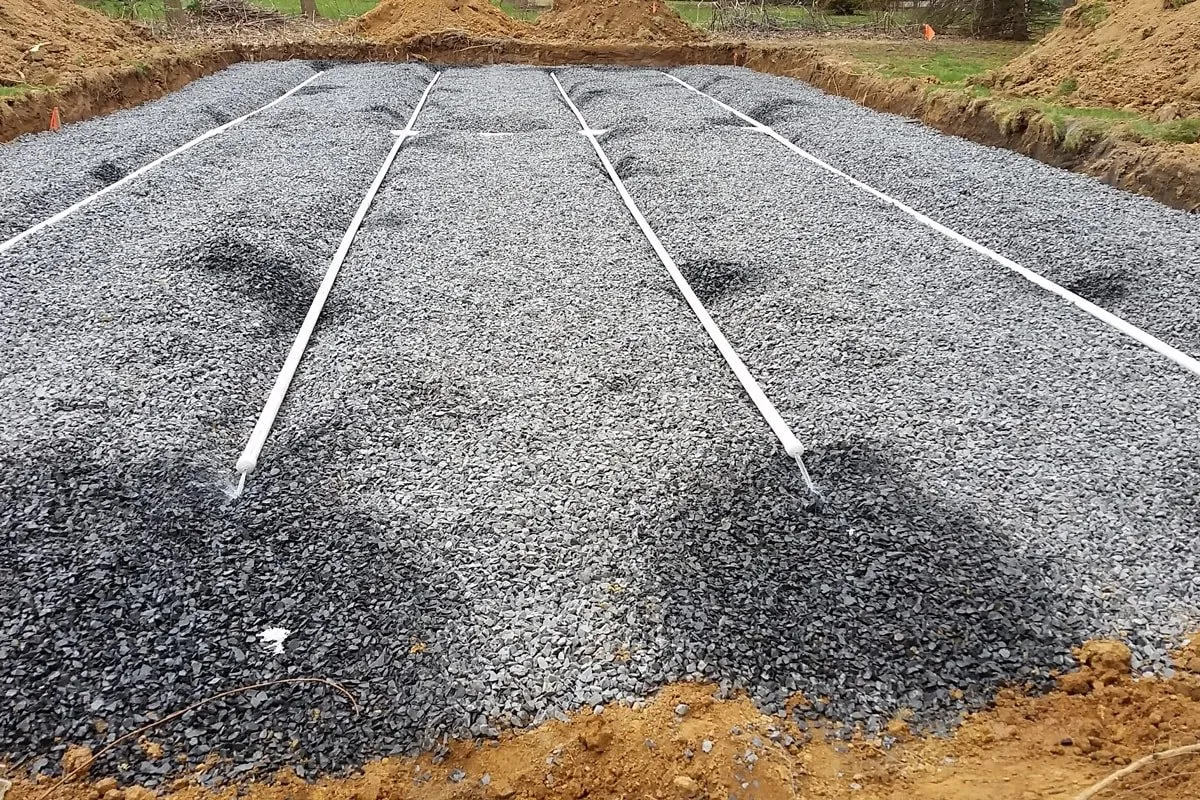 New septic drain field of crushed gravel with white distribution pipes laid in rows inside an excavated bed — cover image for the Damiani Septic website project