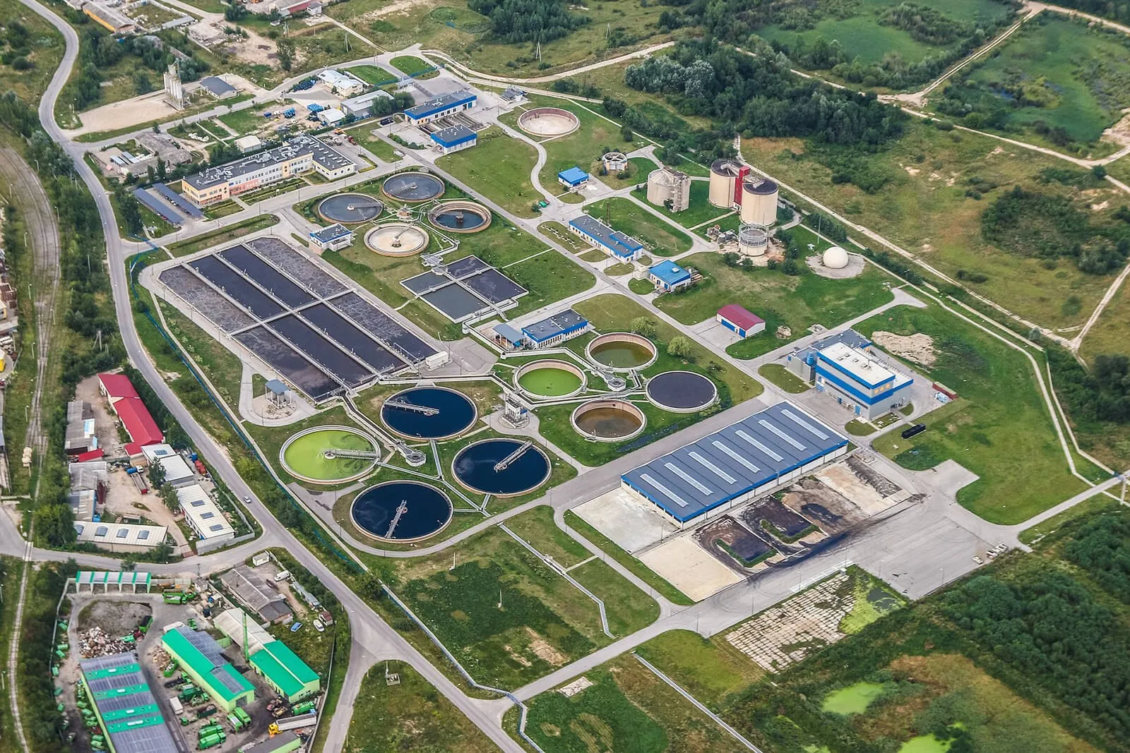 Aerial view of a wastewater treatment plant with round clarifier tanks and settling basins set among green fields — cover image for the EnviroCert International website project