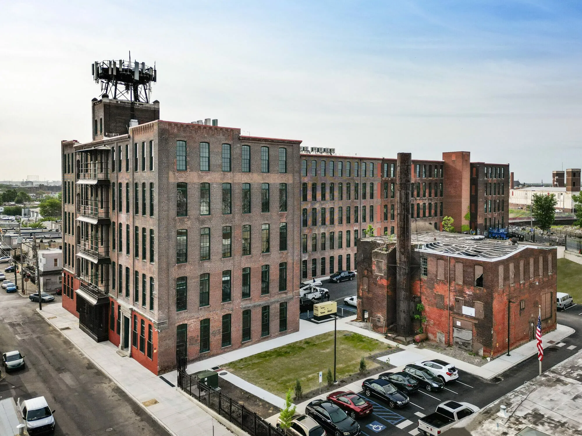 Aerial view of a restored five-story brick mill with tall arched windows beside an older brick boiler house and smokestack — cover image for the McHugh Engineering website project