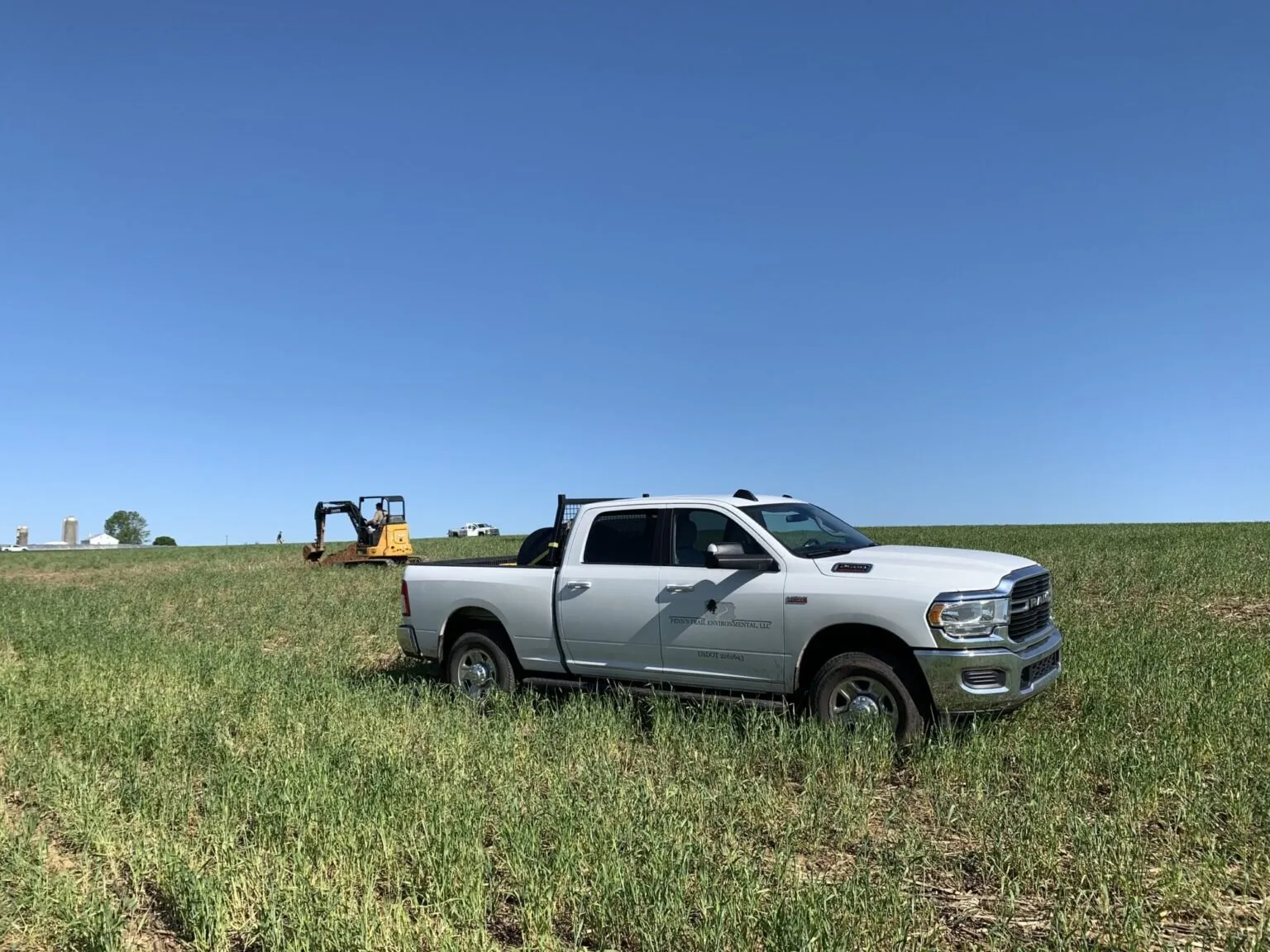 White Penn's Trail Environmental pickup truck parked in a green field under a clear blue sky, with an excavator digging a test pit behind it — cover image for the Penn's Trail Environmental website project