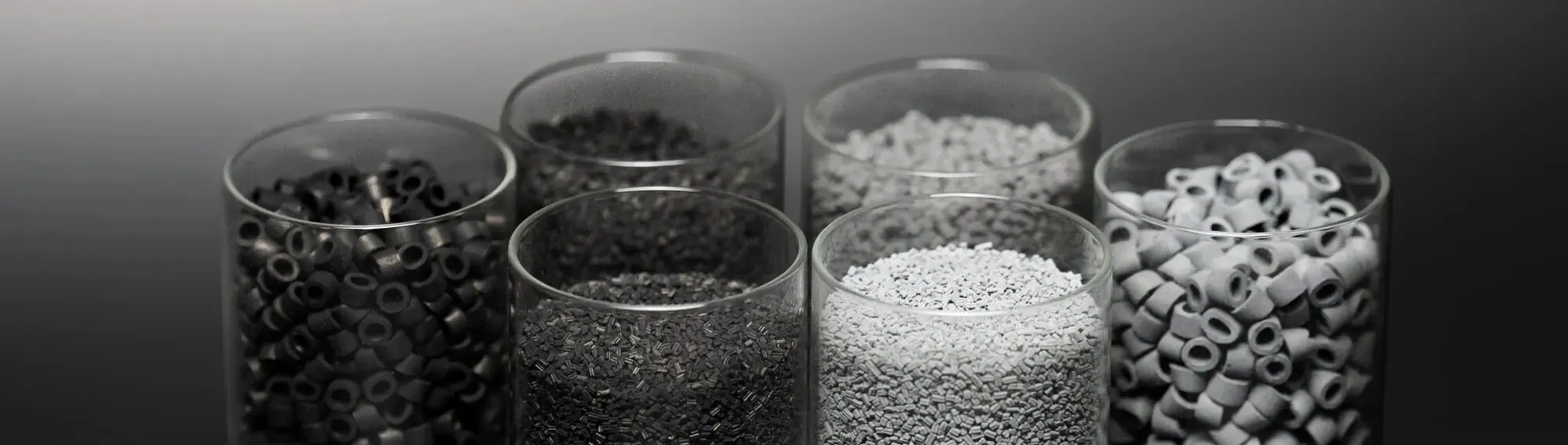 Glass beakers filled with black and white catalyst carrier pellets and rings against a gray background — cover image for the SiCat Catalyst website project