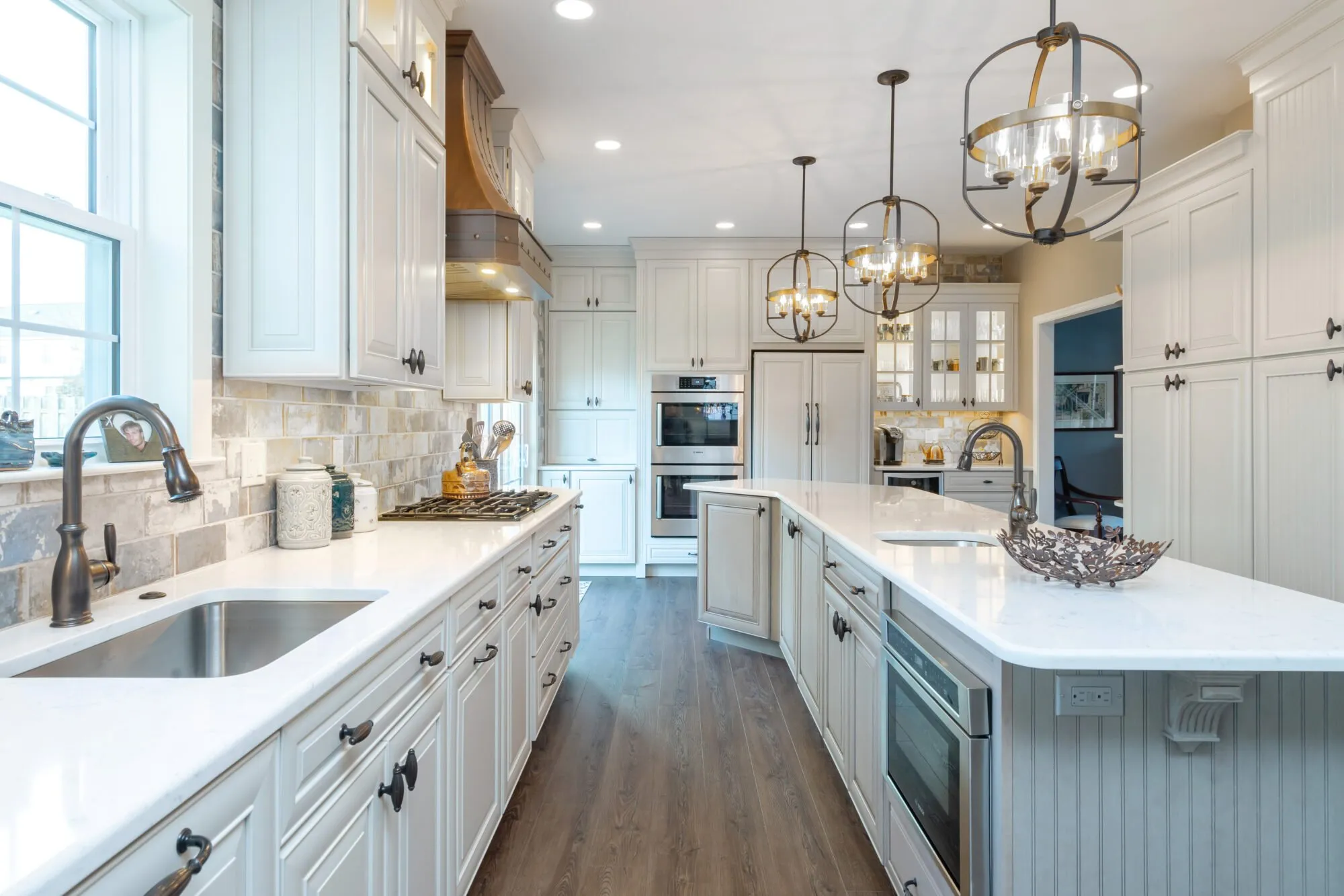 Remodeled white kitchen with a long quartz-topped island, lantern pendants, and wood-look floors — cover image for the Volpe Design Build website project